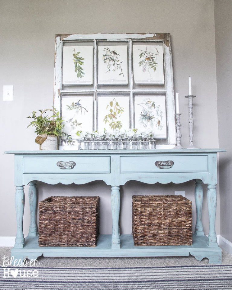 Entrance table in eggshell blue with candlesticks, baskets and distressed picture frame. 