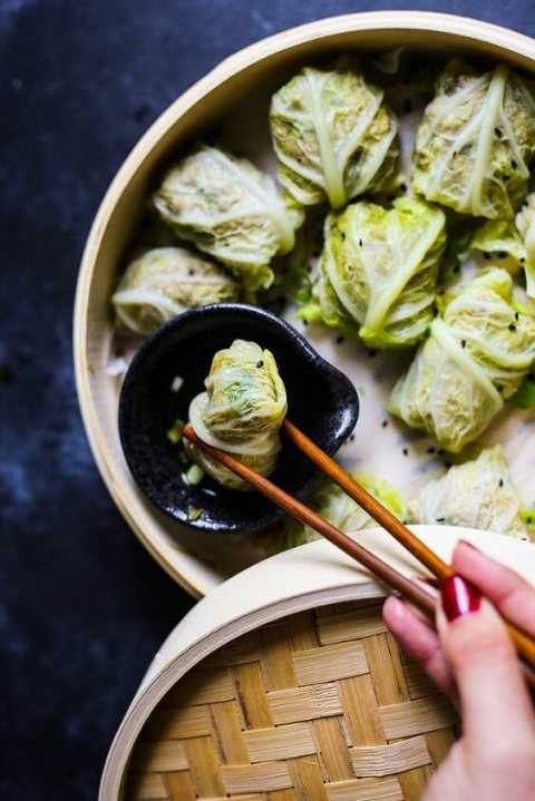 Cabbage pork dumplings held with chopsticks dipping in a sauce. 